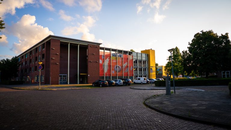 Modern gebouw met kleurrijke gevel en omliggende bomen en parkeerplaatsen.