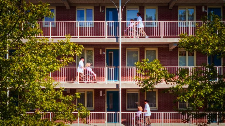 Mensen met en zonder rolstoel bewegen zich op een balkon van een appartementencomplex.